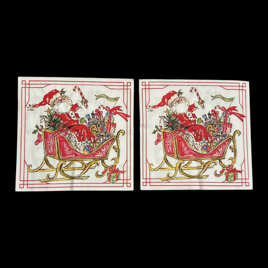 Two Luncheon size decoupage napkin featuring Santa Claus in a red sleigh filled with gifts, candy canes, and holly, bordered in red and gold for Christmas crafts.