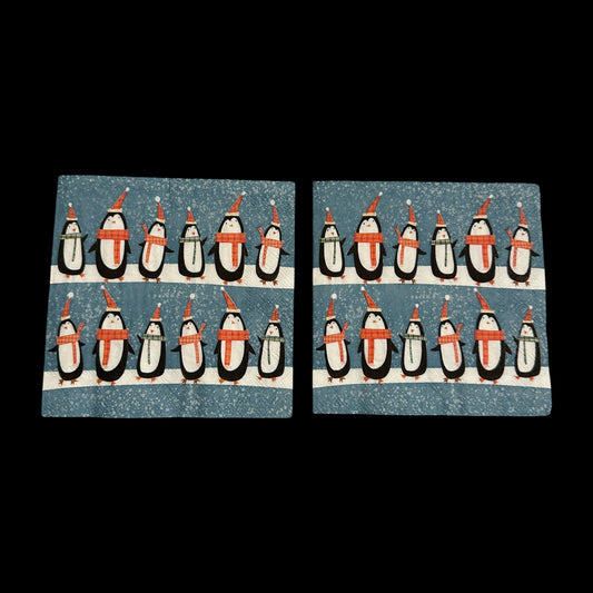 Cocktail size decoupage napkin featuring two rows of adorable black and white penguins in red Santa hats and plaid scarves marching across a snowy blue speckled background set of 2