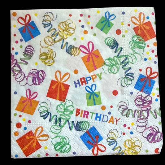 Cocktail-size decoupage paper napkin featuring a lively all-over tossed print of colorful wrapped gift boxes with curly ribbon bows spiraling party streamers multicolor confetti dots and Happy Birthday lettering in bold multicolor text on a crisp white background, photographed on a warm wood surface.