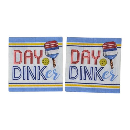 Two cocktail-size decoupage paper napkins featuring a bold graphic design with the phrase DAY DINKer in red and navy lettering alongside a red white and blue pickleball paddle and yellow ball, framed by periwinkle blue and yellow stripe borders on a white background, photographed on a white wall
