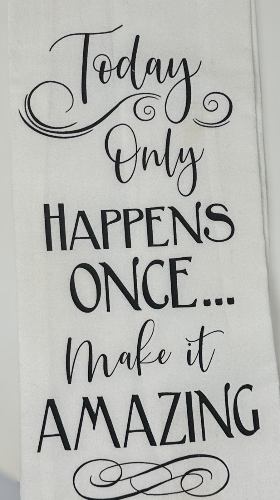 A white flour sack towel with black text textual design saying 'Only Happens Once... Make it Amazing'.