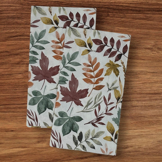 Two decoupage paper napkins with watercolor fall leaves prints in burgundy, green, orange, and gold, fanned out against a beige background.
