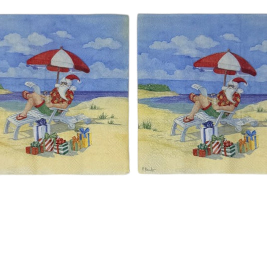 Cocktail-size decoupage paper napkin featuring an illustrated scene of Santa Claus relaxing in a beach lounge chair under a red and white striped umbrella wearing a Hawaiian shirt and flip flops with colorful wrapped gifts in the sand and a bright blue ocean in the background.