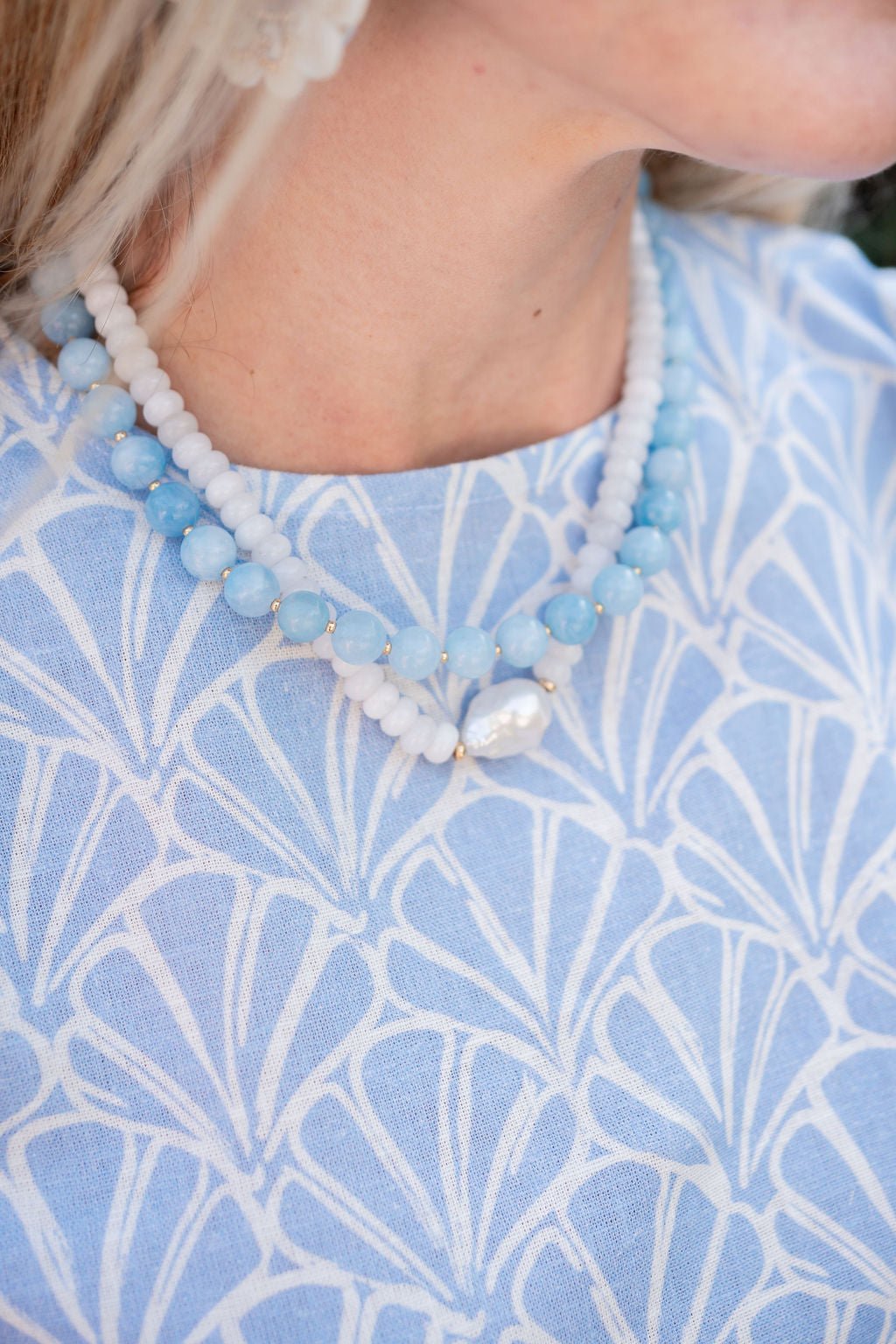 Close-up of a person wearing a blue and white beaded necklace with a blue patterned garment.