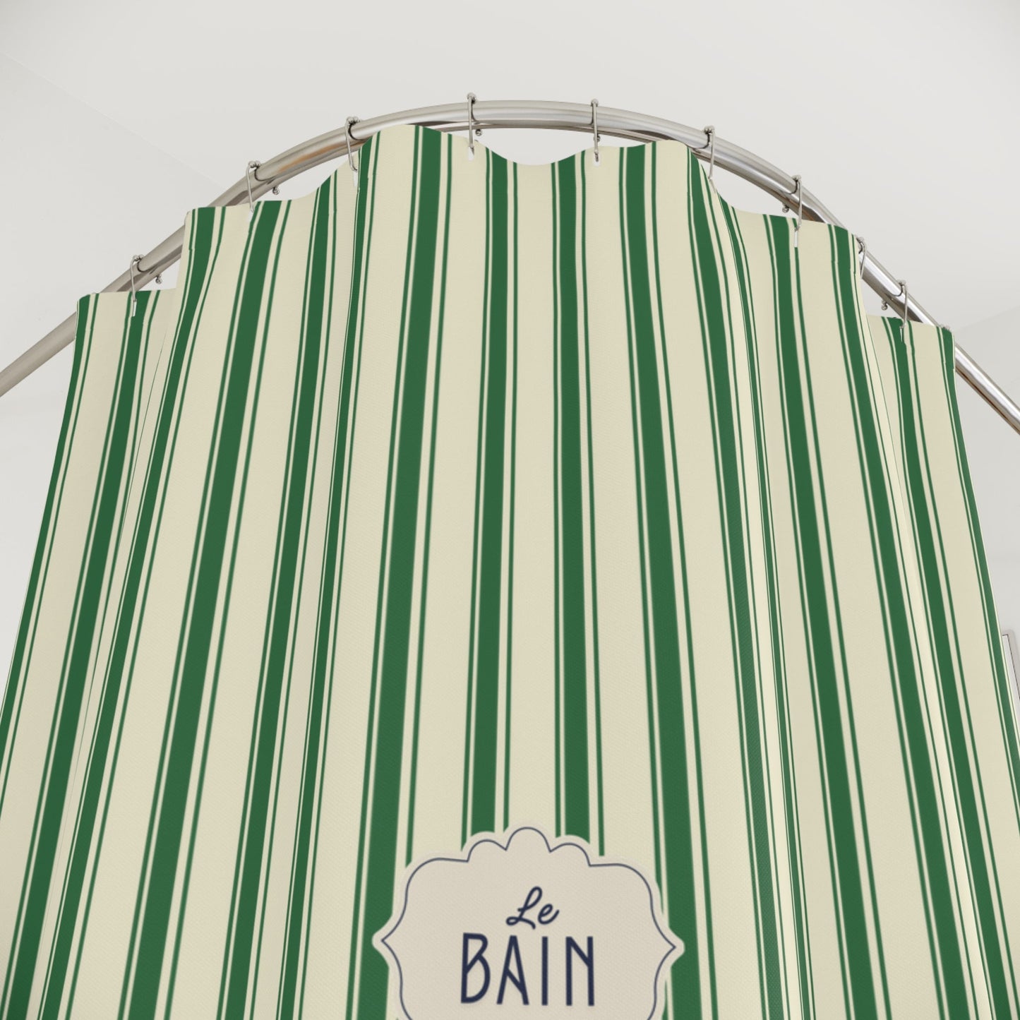 A green and cream vertically striped fabric shower curtain with a decorative white label reading 'Le Bain' at the bottom, hanging from a curved metal rod against a plain light background.