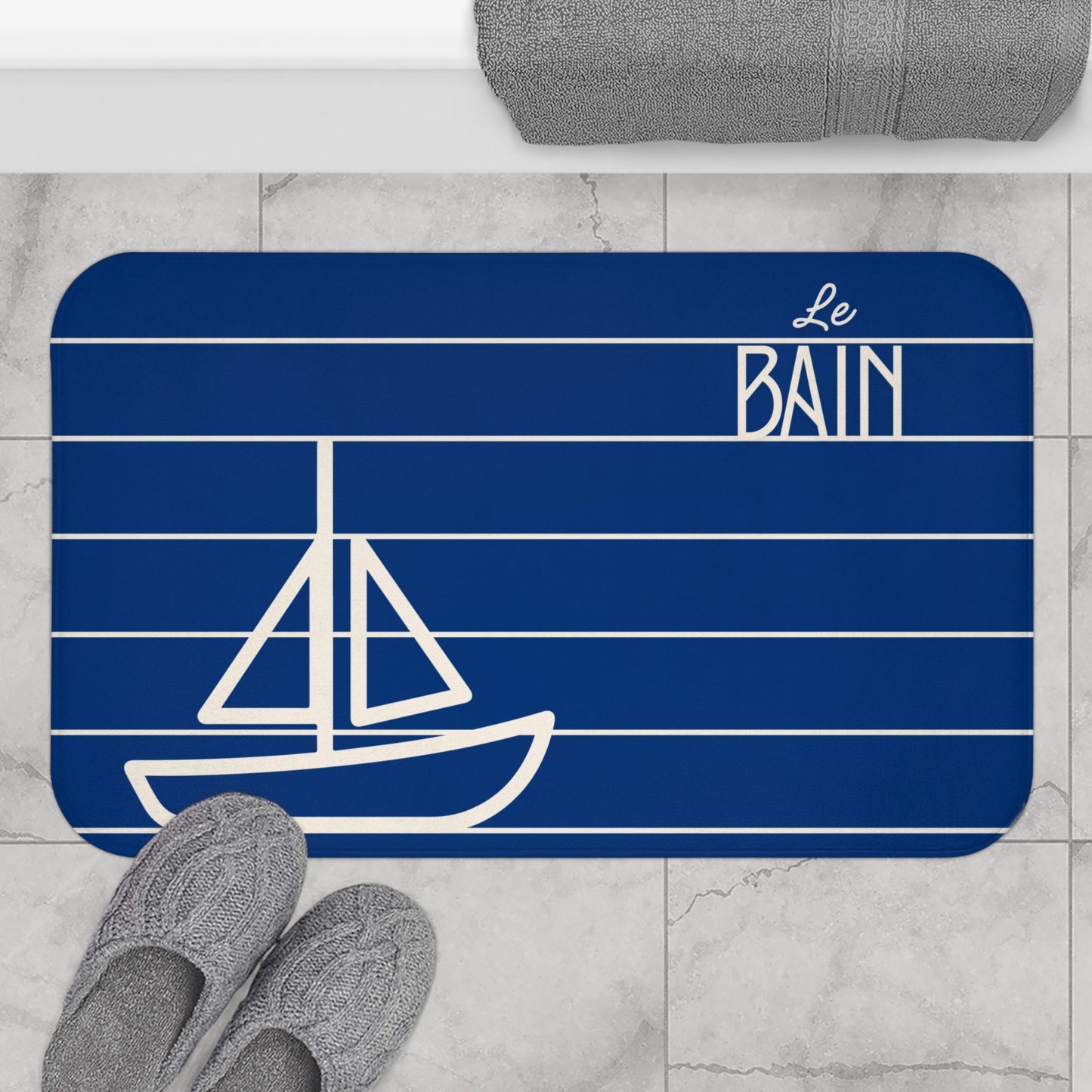 Bath mat with sailboat design and 'Le Bain' text on a marble floor.
