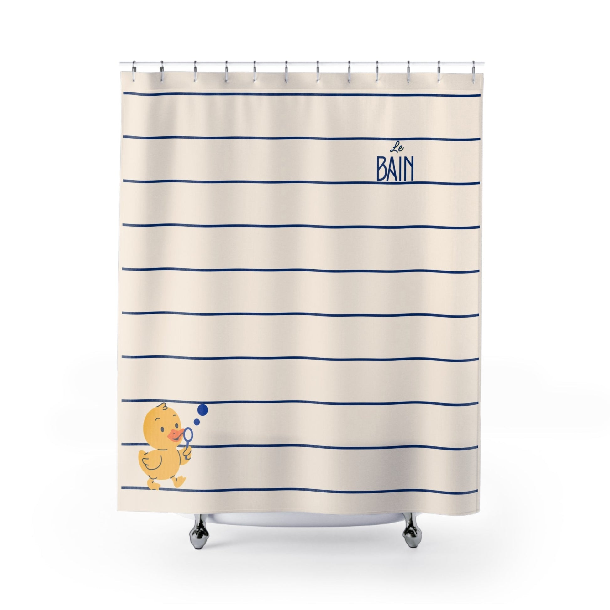 An off-white shower curtain with horizontal navy blue stripes, featuring the French text 'le BAIN' in navy near the top right and a small yellow rubber duck blowing bubbles near the bottom left. The curtain is hanging from silver rings on a white rod, with the feet of silver tub wheels visible at the bottom against a clean white background.