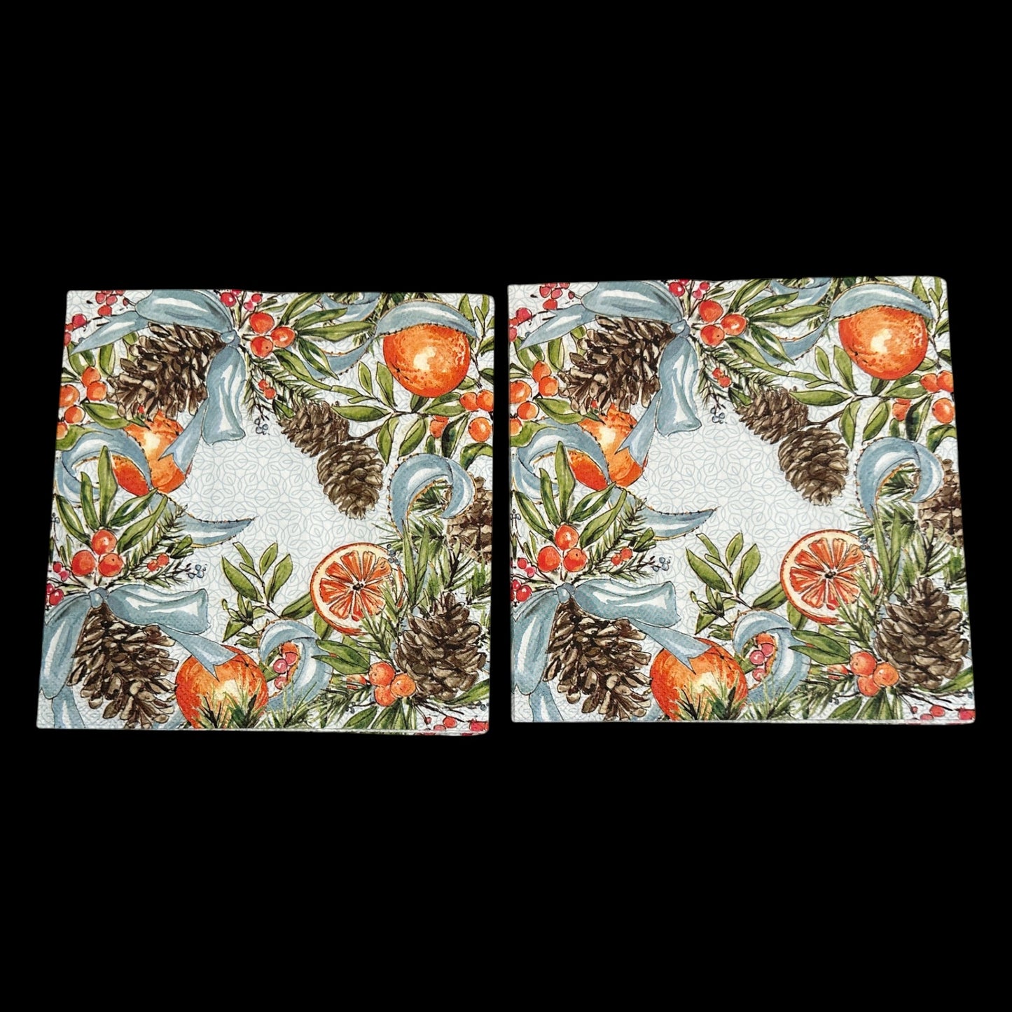 Two Luncheon size decoupage napkin featuring pinecones, oranges, citrus slices, red berries, and blue ribbons on a white patterned background for holiday crafts.