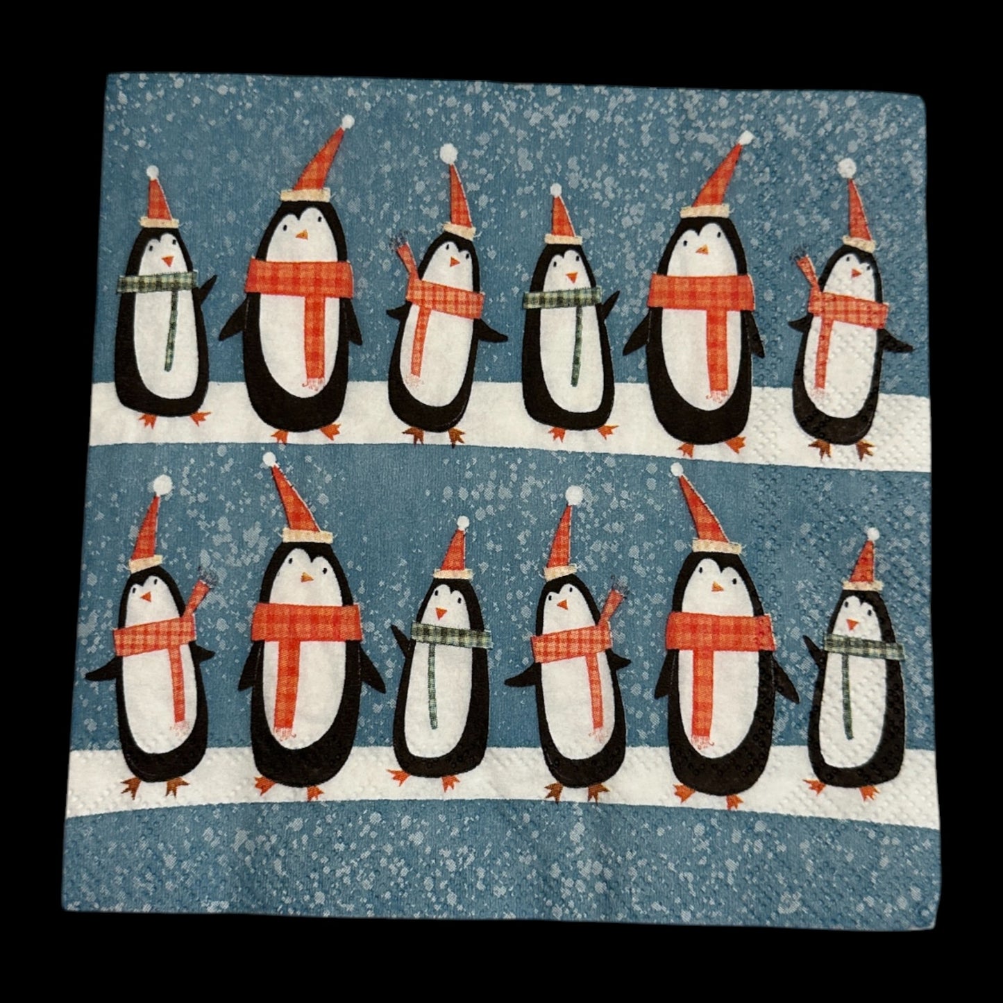 Cocktail size decoupage napkin featuring rows of cute penguins wearing scarves and Santa hats on a snowy blue background for holiday crafts and decor.