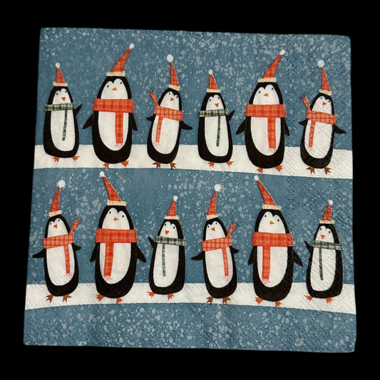 Cocktail size decoupage napkin featuring two rows of adorable black and white penguins in red Santa hats and plaid scarves marching across a snowy blue speckled background set of 2