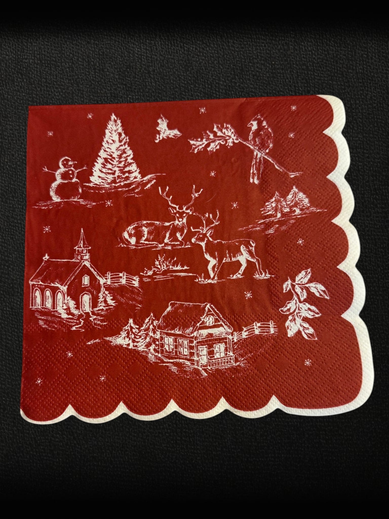 Cocktail size decoupage napkin with scalloped white edge featuring a classic red and white Christmas winter toile scene with snowman deer church cabin cardinal and holly sprigs set of 2