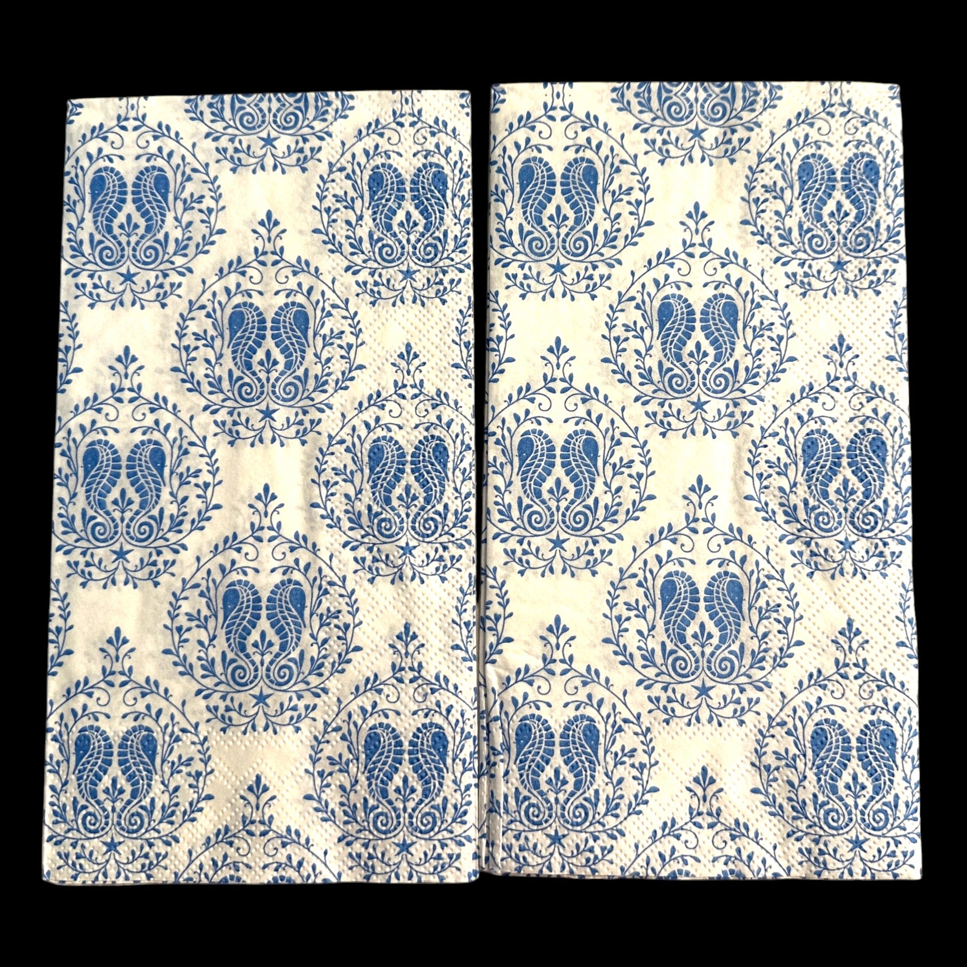 Two guest-size decoupage paper napkins featuring a detailed all-over print of classic paisley teardrops with intricate interior scrollwork and trailing vine and leaf sprigs in rich cobalt and periwinkle blue on a soft warm white background, photographed on a light grey surface.