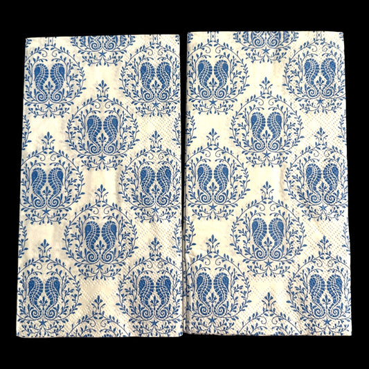 Two guest-size decoupage paper napkins featuring a detailed all-over print of classic paisley teardrops with intricate interior scrollwork and trailing vine and leaf sprigs in rich cobalt and periwinkle blue on a soft warm white background, photographed on a light grey surface.