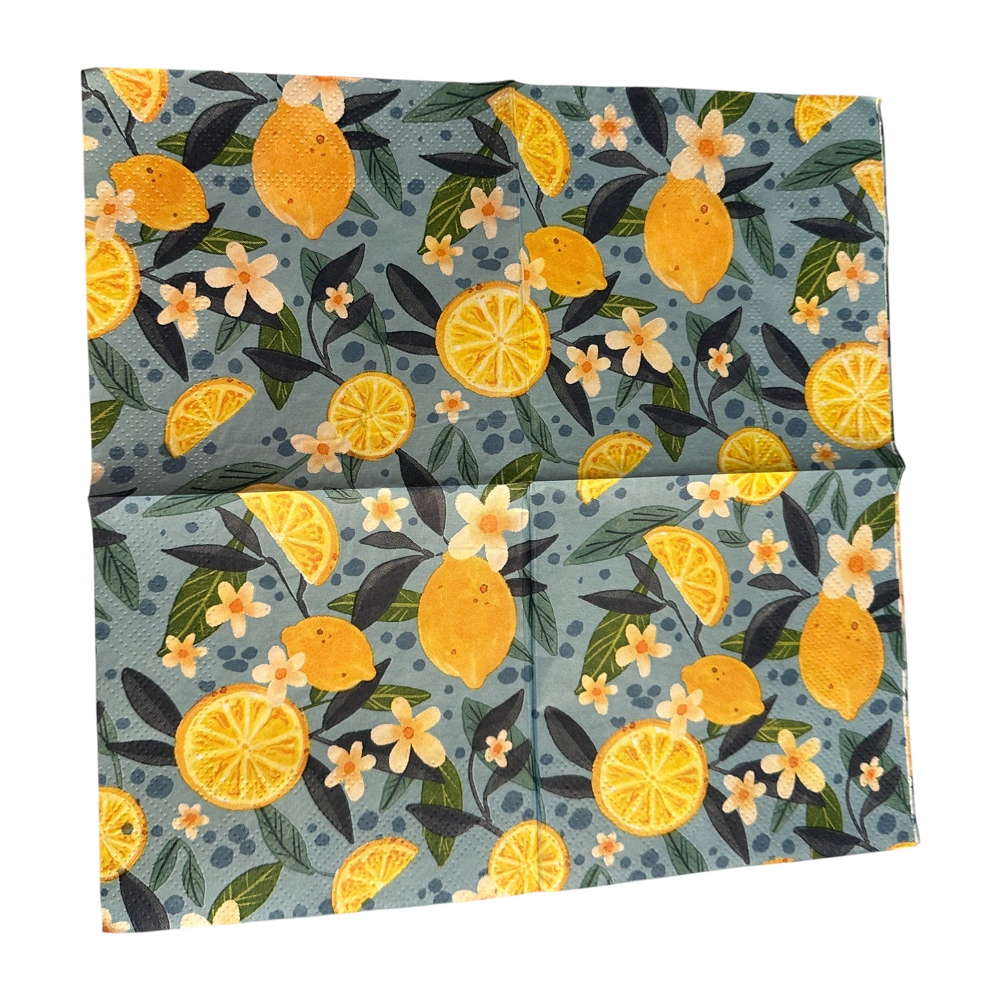 Cocktail-size decoupage paper napkin featuring a lush all-over botanical print of golden whole lemons and halved citrus slices with white orange blossom flowers and rich dark and forest green leaves on a soft dusty blue background with subtle dot accents, photographed on a black surface.