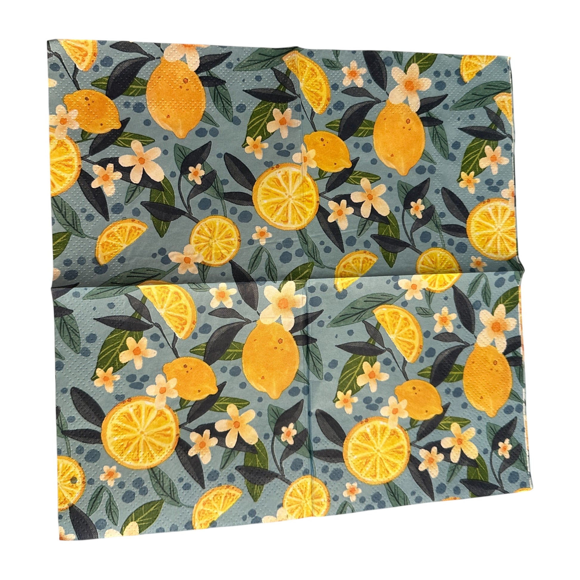 Cocktail-size decoupage paper napkin featuring a lush all-over botanical print of golden whole lemons and halved citrus slices with white orange blossom flowers and rich dark and forest green leaves on a soft dusty blue background with subtle dot accents, photographed on a black surface.