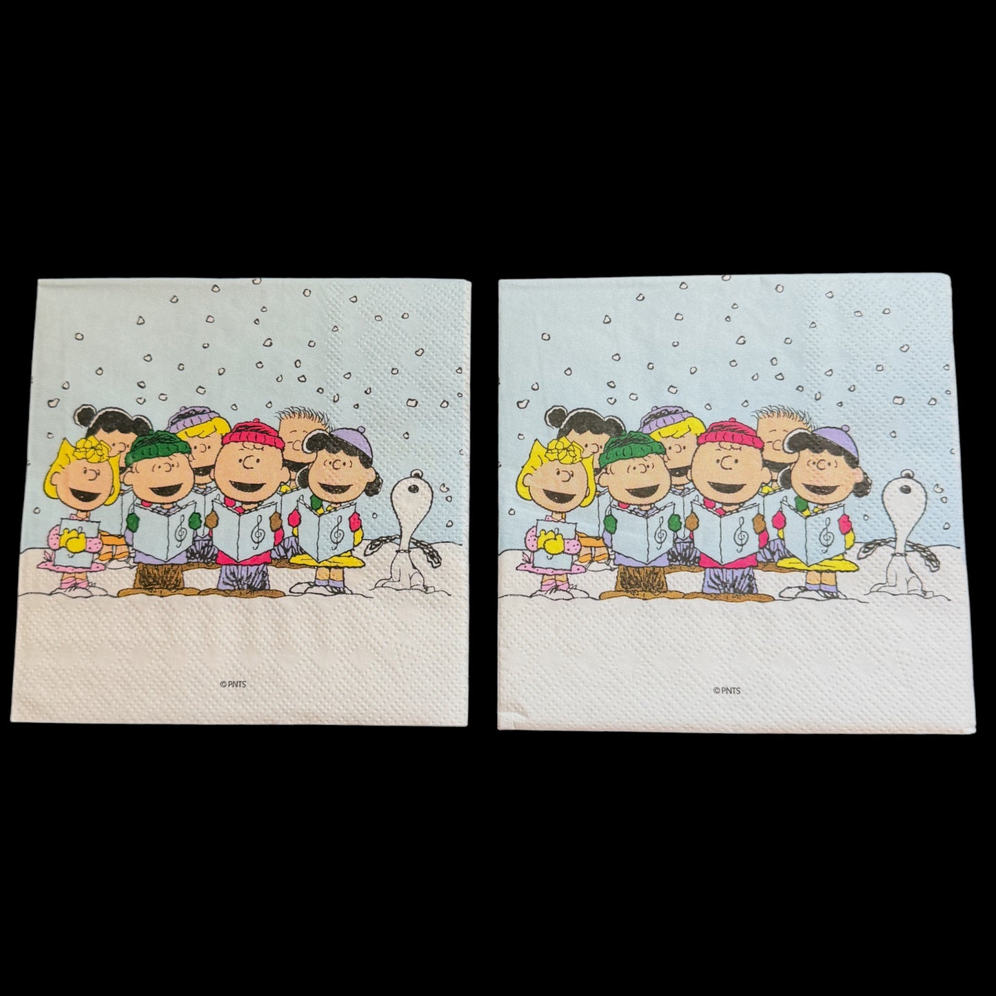 Cocktail size decoupage napkin featuring the Peanuts gang including Charlie Brown Snoopy Lucy Sally and friends caroling together in falling snow on a soft blue winter background set of 2