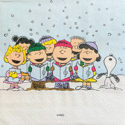 Cocktail size decoupage napkin featuring the Peanuts gang including Charlie Brown Snoopy Lucy Sally and friends caroling together in falling snow on a soft blue winter background set of 2