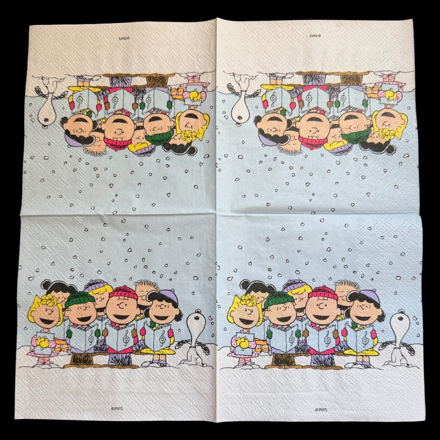 Cocktail size decoupage napkin featuring the Peanuts gang including Charlie Brown Snoopy Lucy Sally and friends caroling together in falling snow on a soft blue winter background set of 2