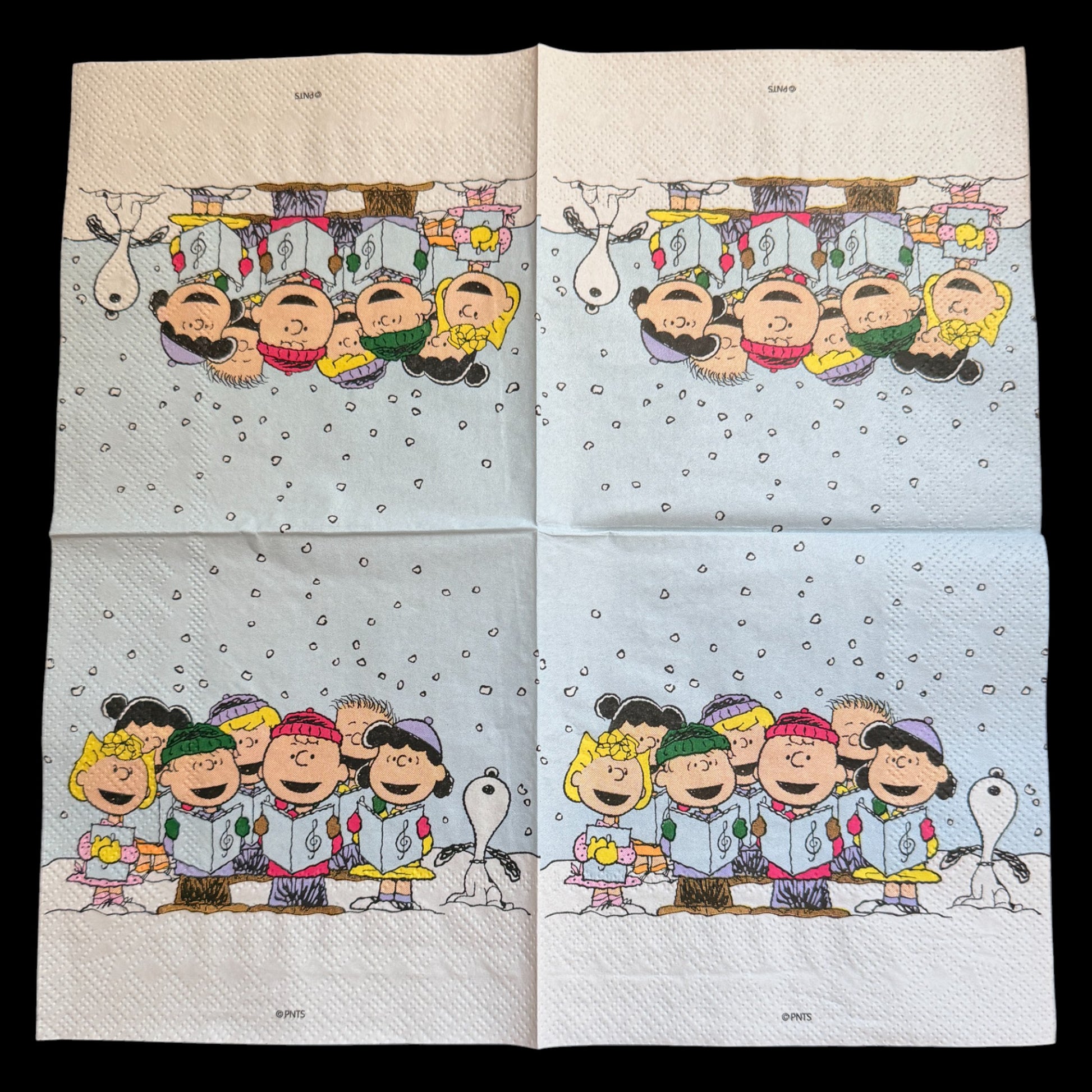Cocktail size decoupage napkin featuring the Peanuts gang including Charlie Brown Snoopy Lucy Sally and friends caroling together in falling snow on a soft blue winter background set of 2