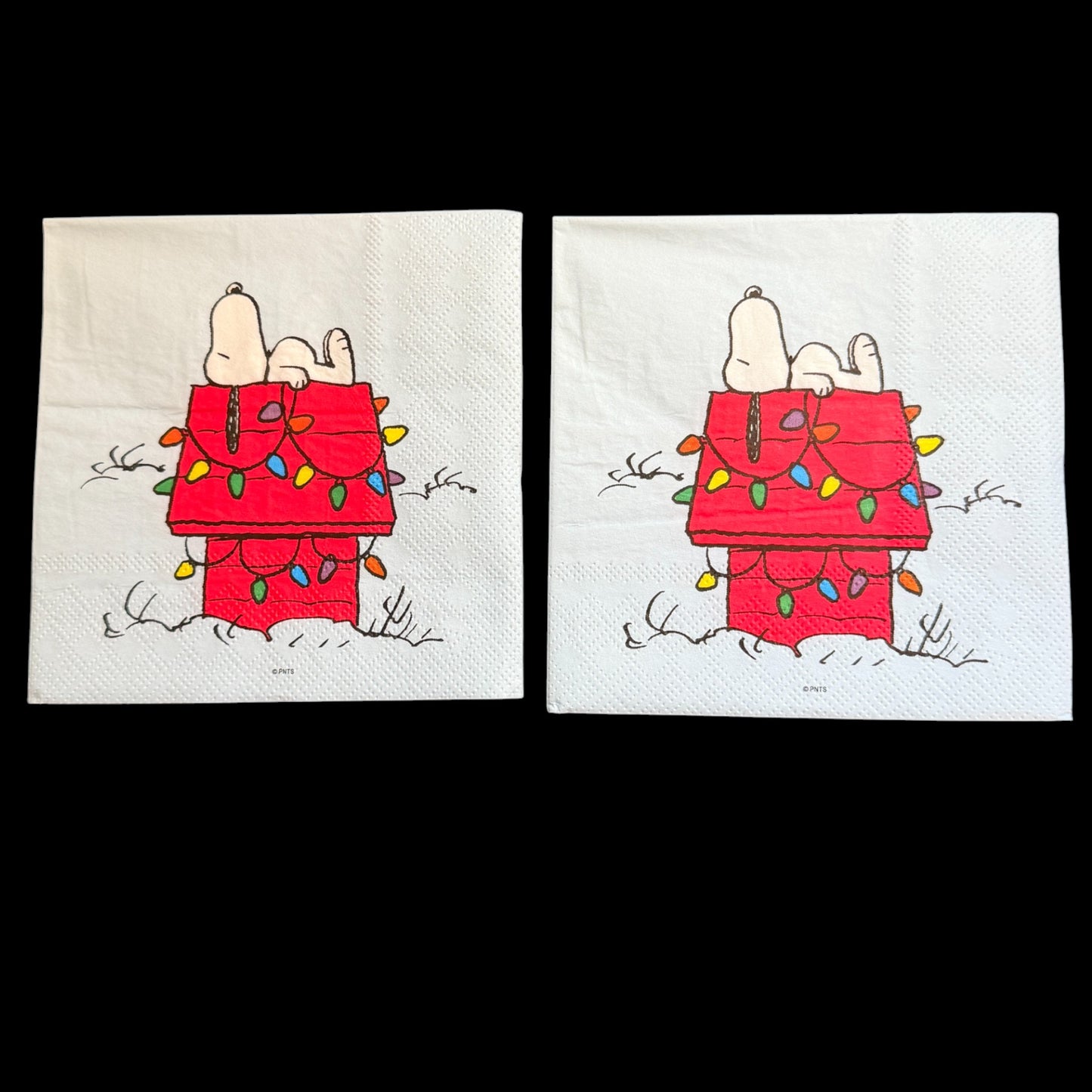 Cocktail size decoupage napkin featuring Snoopy lounging on his red dog house wrapped in colorful multicolored Christmas lights on a white winter background set of 2