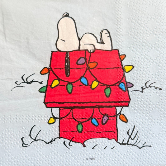 Cocktail size decoupage napkin featuring Snoopy lounging on his red dog house wrapped in colorful multicolored Christmas lights on a white winter background set of 2