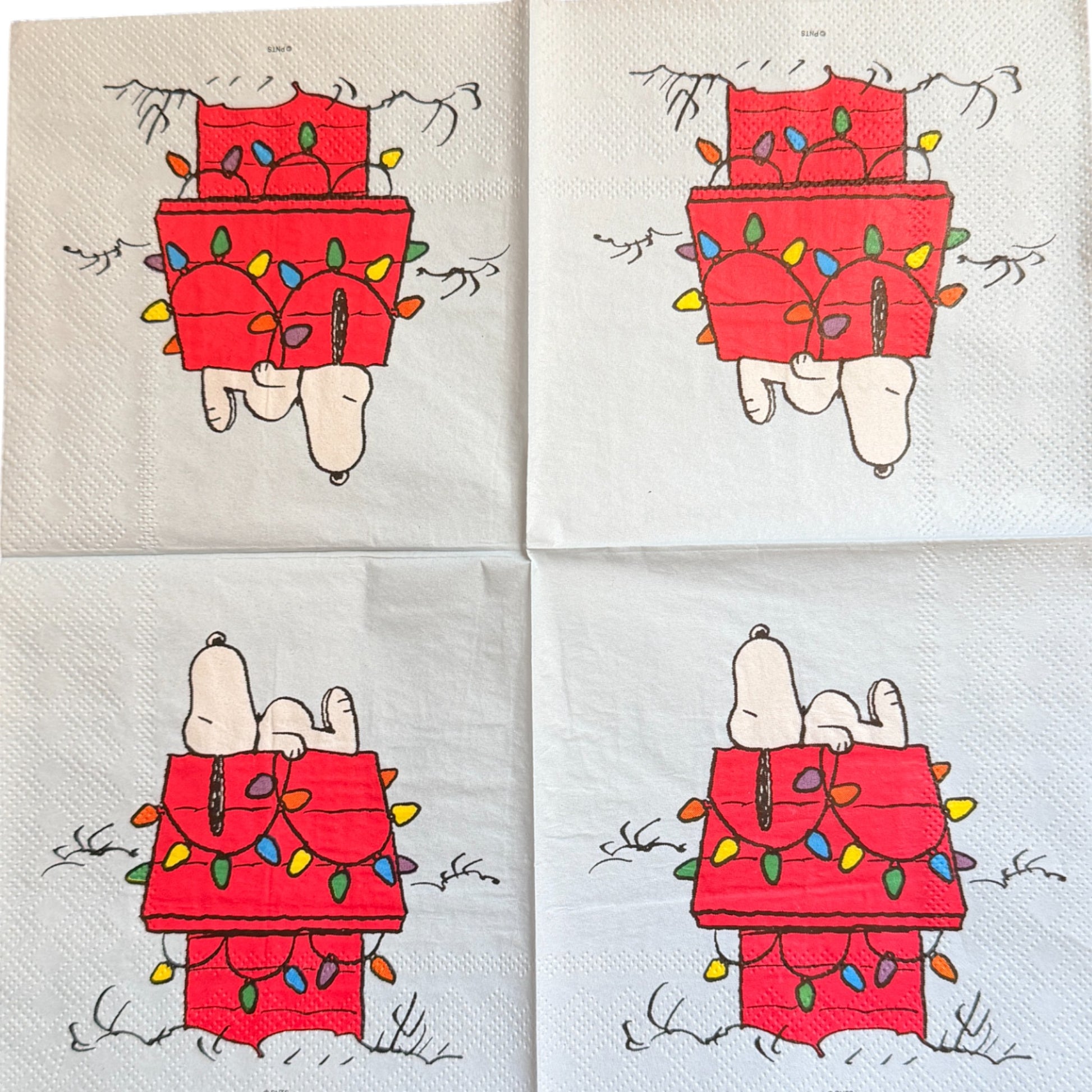 Cocktail size decoupage napkin featuring Snoopy lounging on his red dog house wrapped in colorful multicolored Christmas lights on a white winter background set of 2