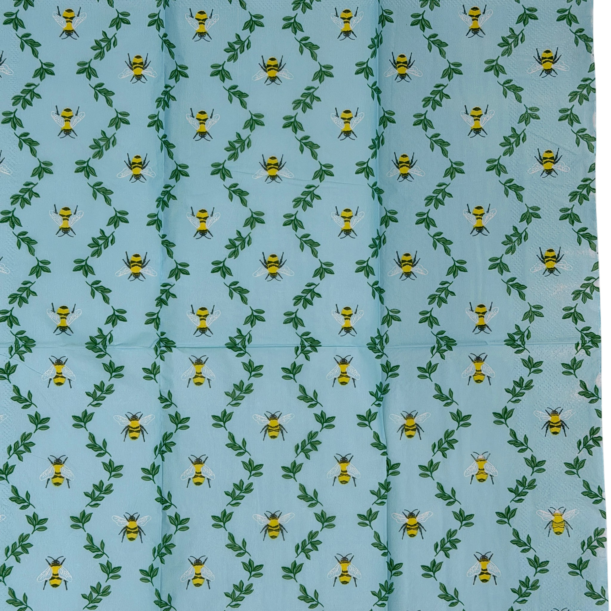 Two guest-size decoupage paper napkins featuring an all-over print of plump yellow and black bumblebees with white wings scattered among delicate green leaf sprigs on a soft sky blue background with a subtle honeycomb texture, photographed on a black surface.