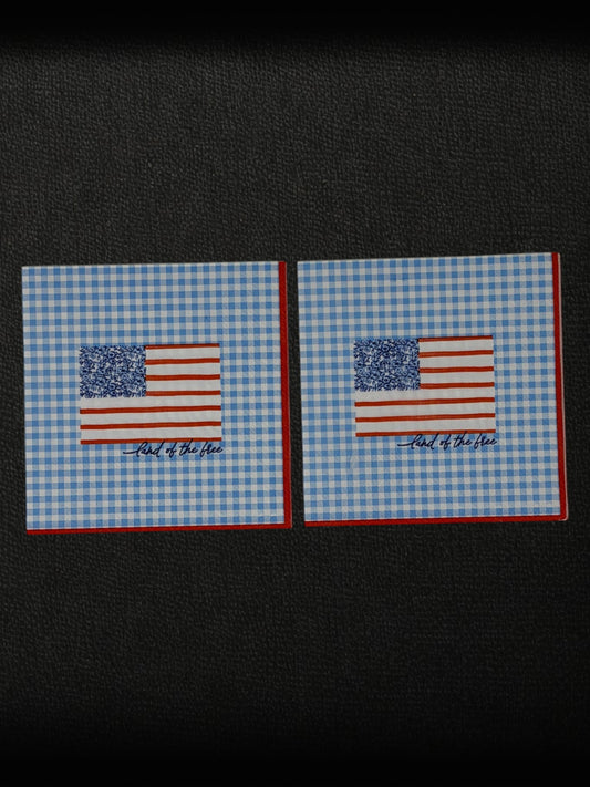 Cocktail size decoupage paper napkin featuring a stylized American flag with a blue floral botanical canton and red stripes above Land of the free cursive script on a fresh sky blue gingham background with a red border set of 2
