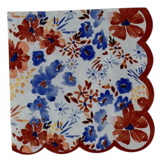 Cocktail-size decoupage paper napkin with a distinctive red scalloped edge featuring a watercolor floral print of cornflower blue blooms, deep rust red flowers, soft blush pink petals, and golden accents on a crisp white background, photographed on a white surface.