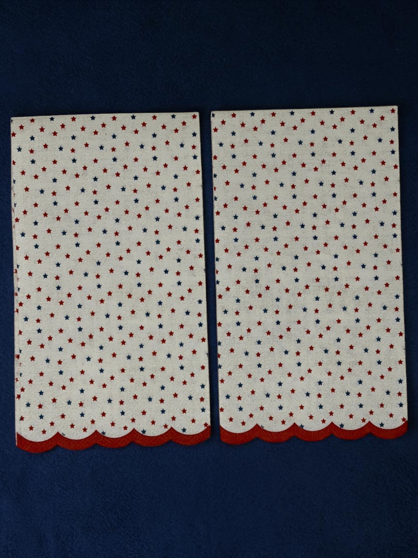 
Guest-size decoupage paper napkin featuring a delicate all-over tossed pattern of tiny red and navy blue stars on a soft warm white background with a charming red scalloped edge border, photographed on a white surface.