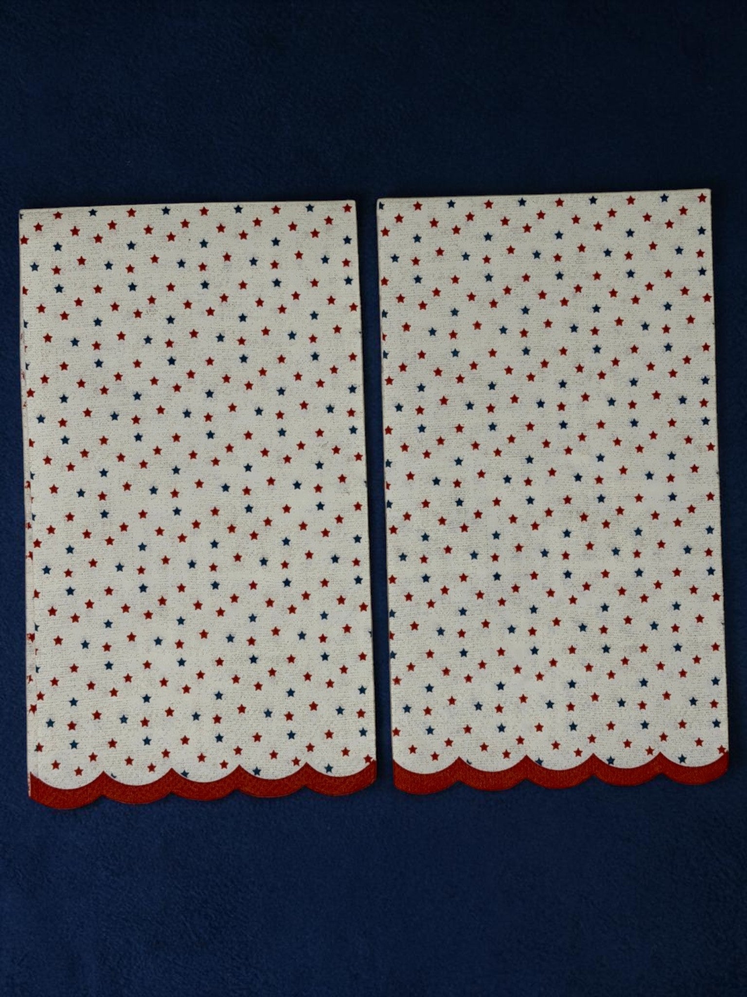 
Guest-size decoupage paper napkin featuring a delicate all-over tossed pattern of tiny red and navy blue stars on a soft warm white background with a charming red scalloped edge border, photographed on a white surface.