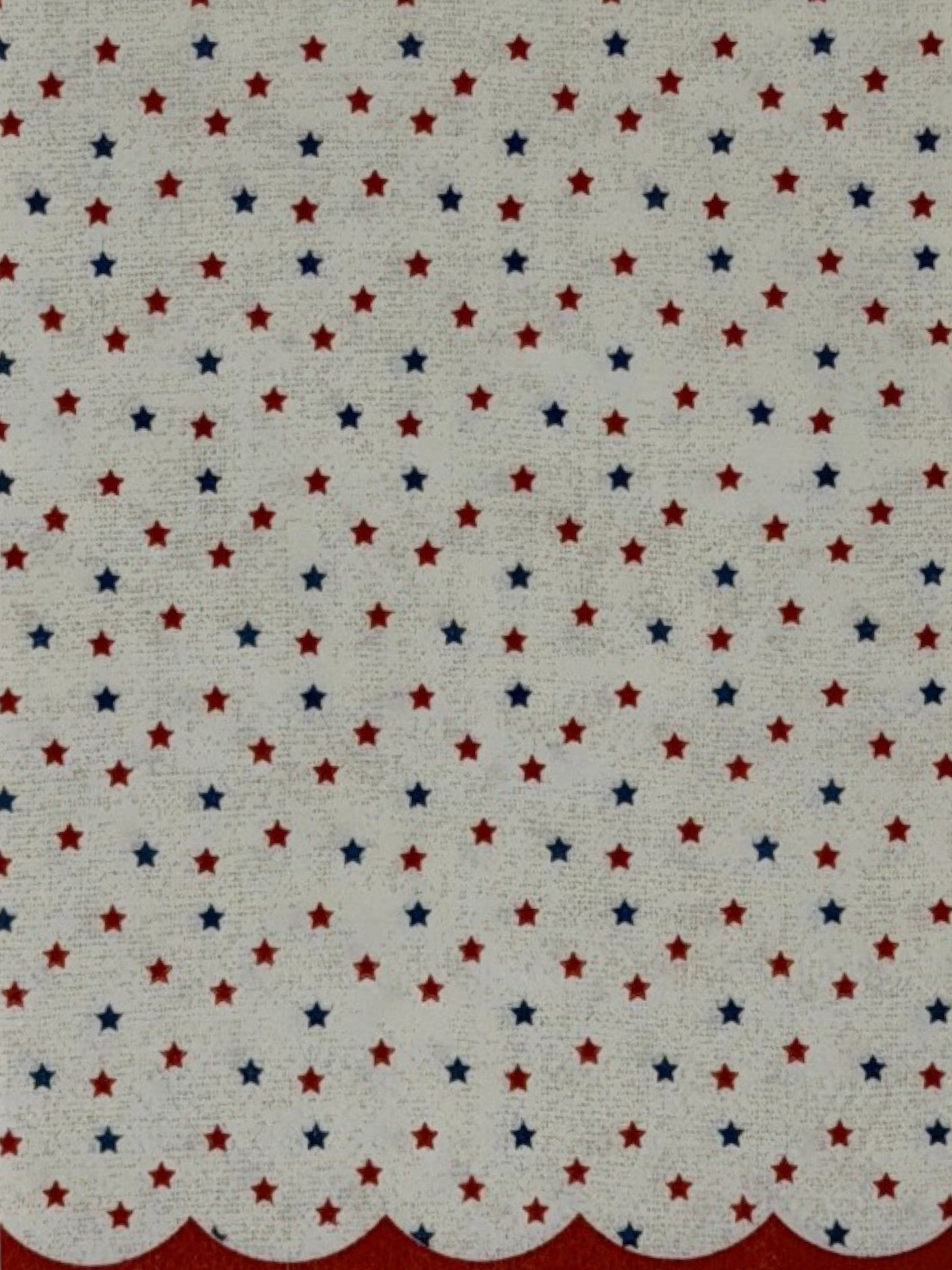 
Guest-size decoupage paper napkin featuring a delicate all-over tossed pattern of tiny red and navy blue stars on a soft warm white background with a charming red scalloped edge border, photographed on a white surface.