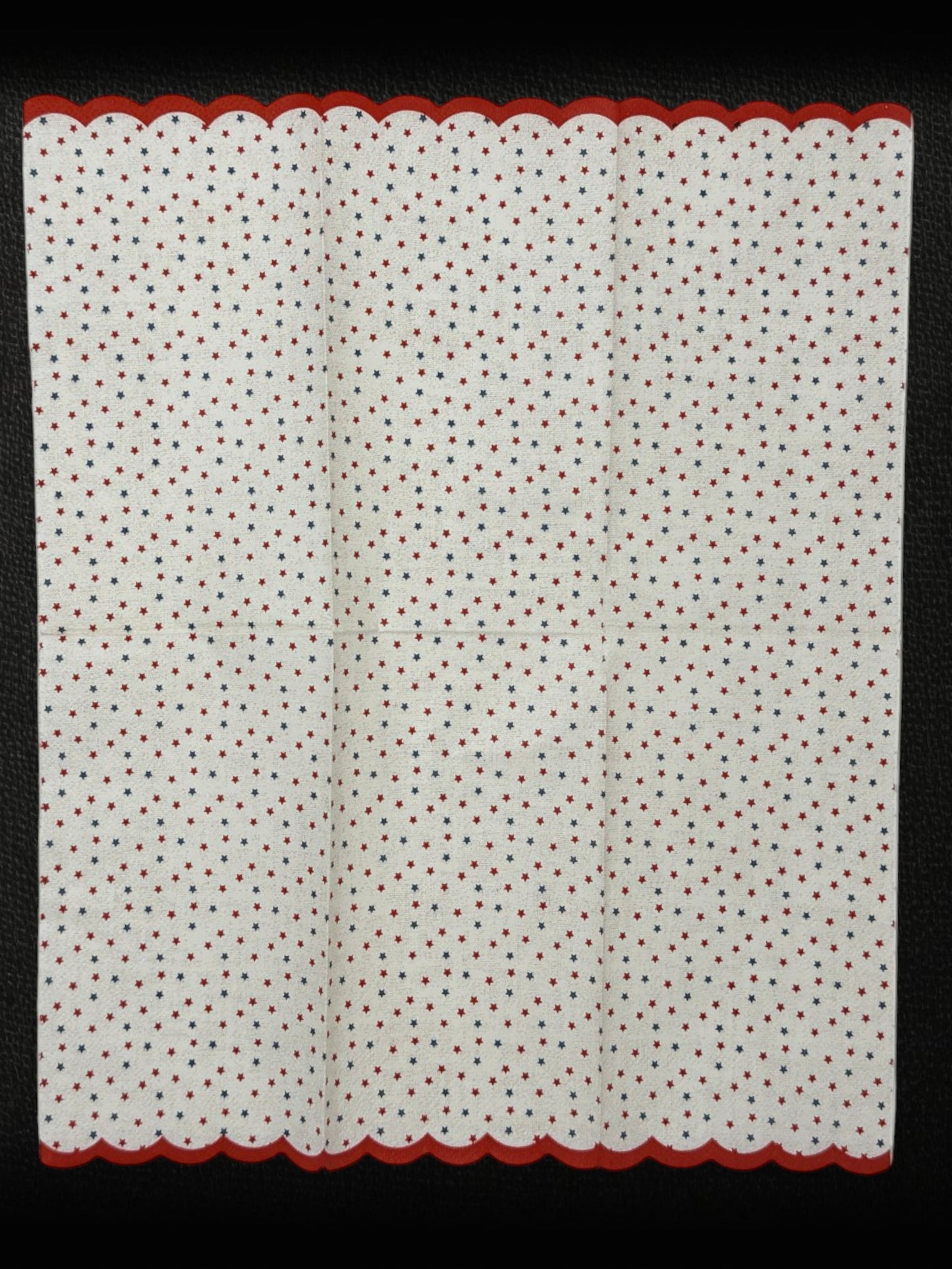 
Guest-size decoupage paper napkin featuring a delicate all-over tossed pattern of tiny red and navy blue stars on a soft warm white background with a charming red scalloped edge border, photographed on a white surface.