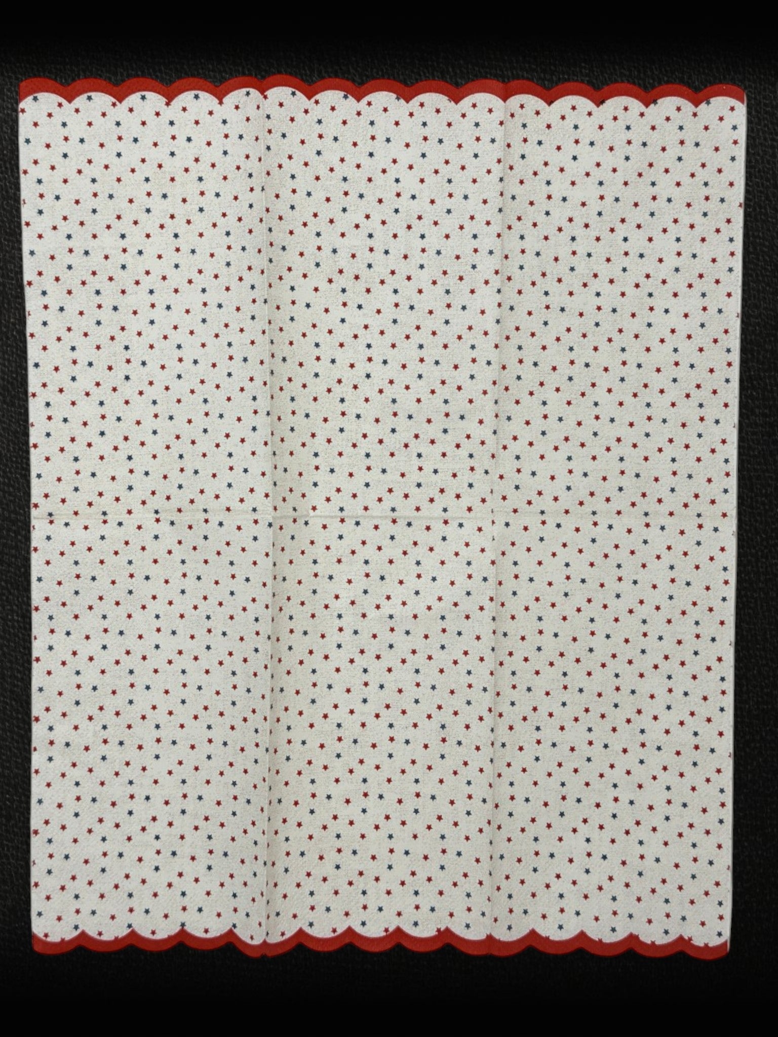 
Guest-size decoupage paper napkin featuring a delicate all-over tossed pattern of tiny red and navy blue stars on a soft warm white background with a charming red scalloped edge border, photographed on a white surface.