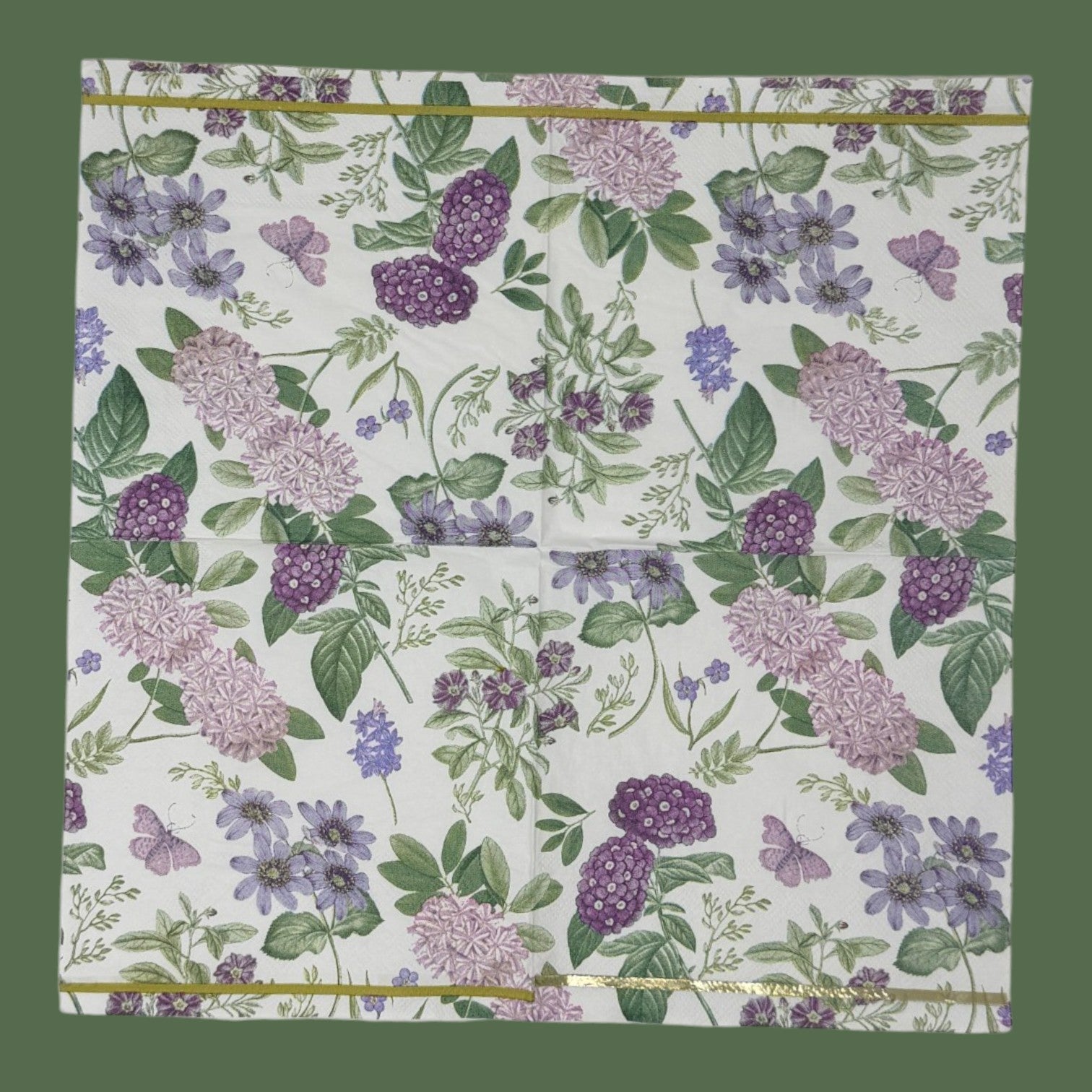 Luncheon-size decoupage paper napkin featuring a vintage botanical illustration print of lavender and purple lilac clusters, periwinkle blue anemones, mauve wildflowers, tiny purple butterflies, and green leaves on a white background with gold foil border stripes, photographed against a white wall.