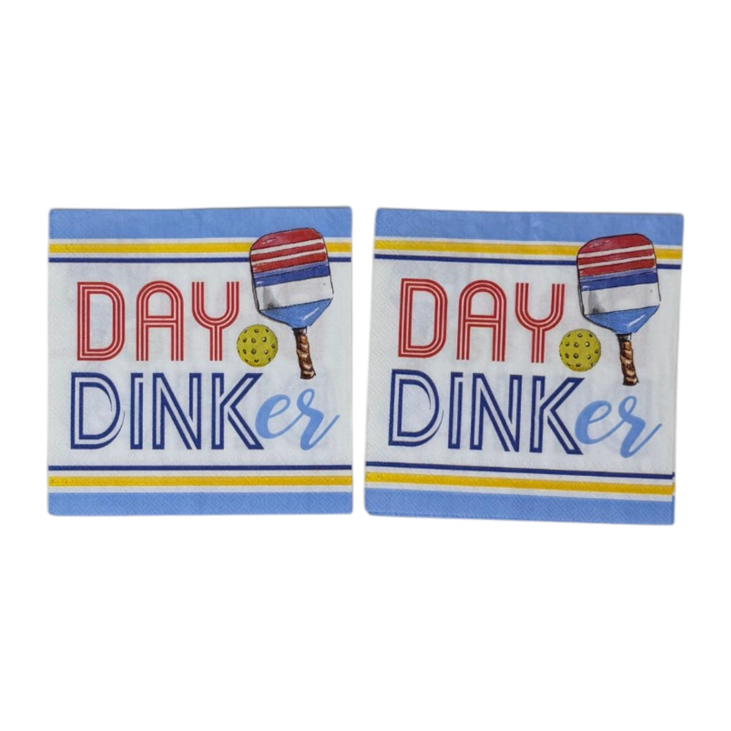 Two cocktail-size decoupage paper napkins featuring a bold graphic design with the phrase DAY DINKer in red and navy lettering alongside a red white and blue pickleball paddle and yellow ball, framed by periwinkle blue and yellow stripe borders on a white background, photographed on a white wall