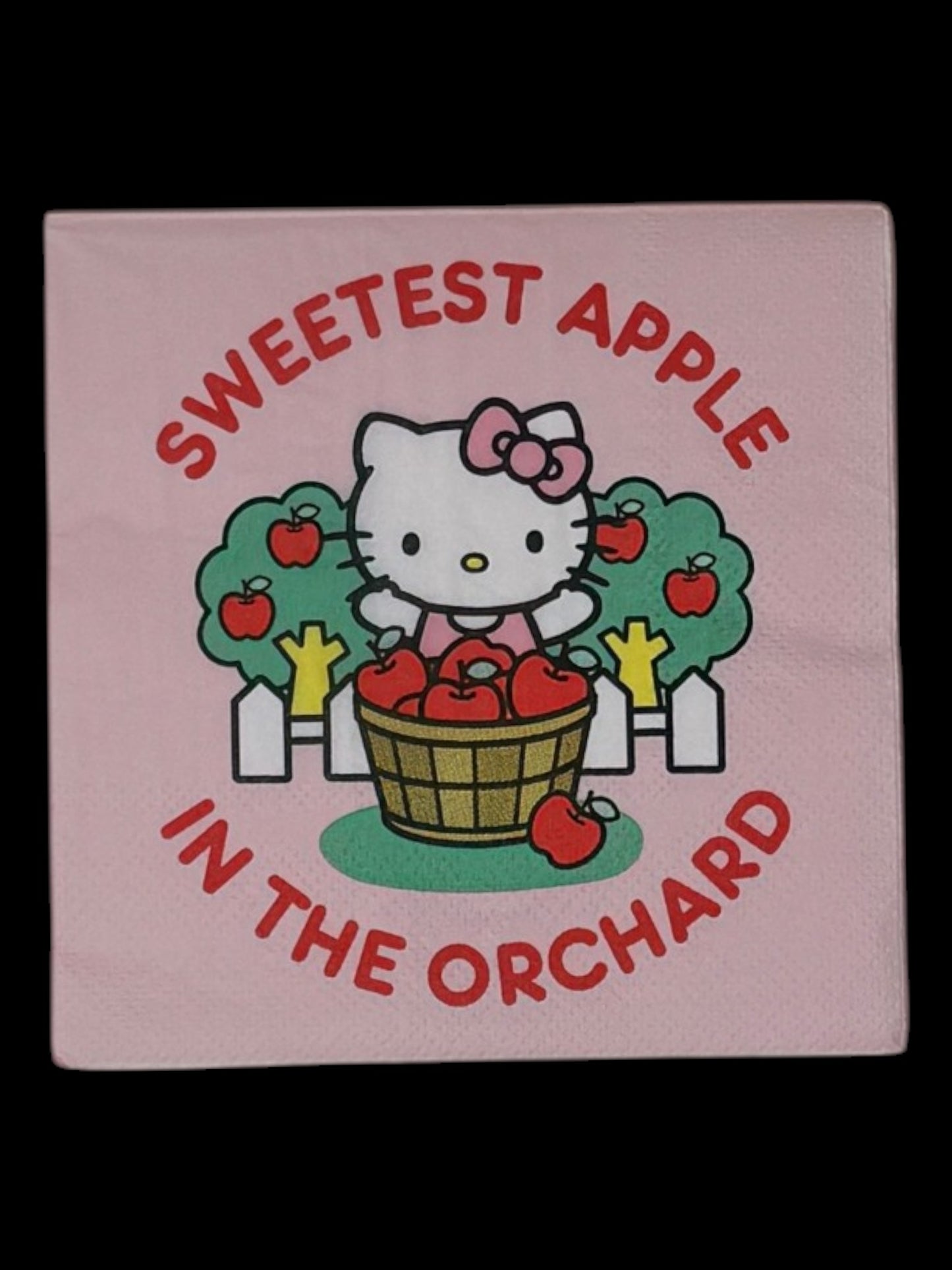 Cocktail-size decoupage paper napkin featuring Hello Kitty standing behind a wooden barrel of red apples with green apple trees and a white picket fence, surrounded by the phrase Sweetest Apple in the Orchard in bold red lettering on a soft blush pink background.