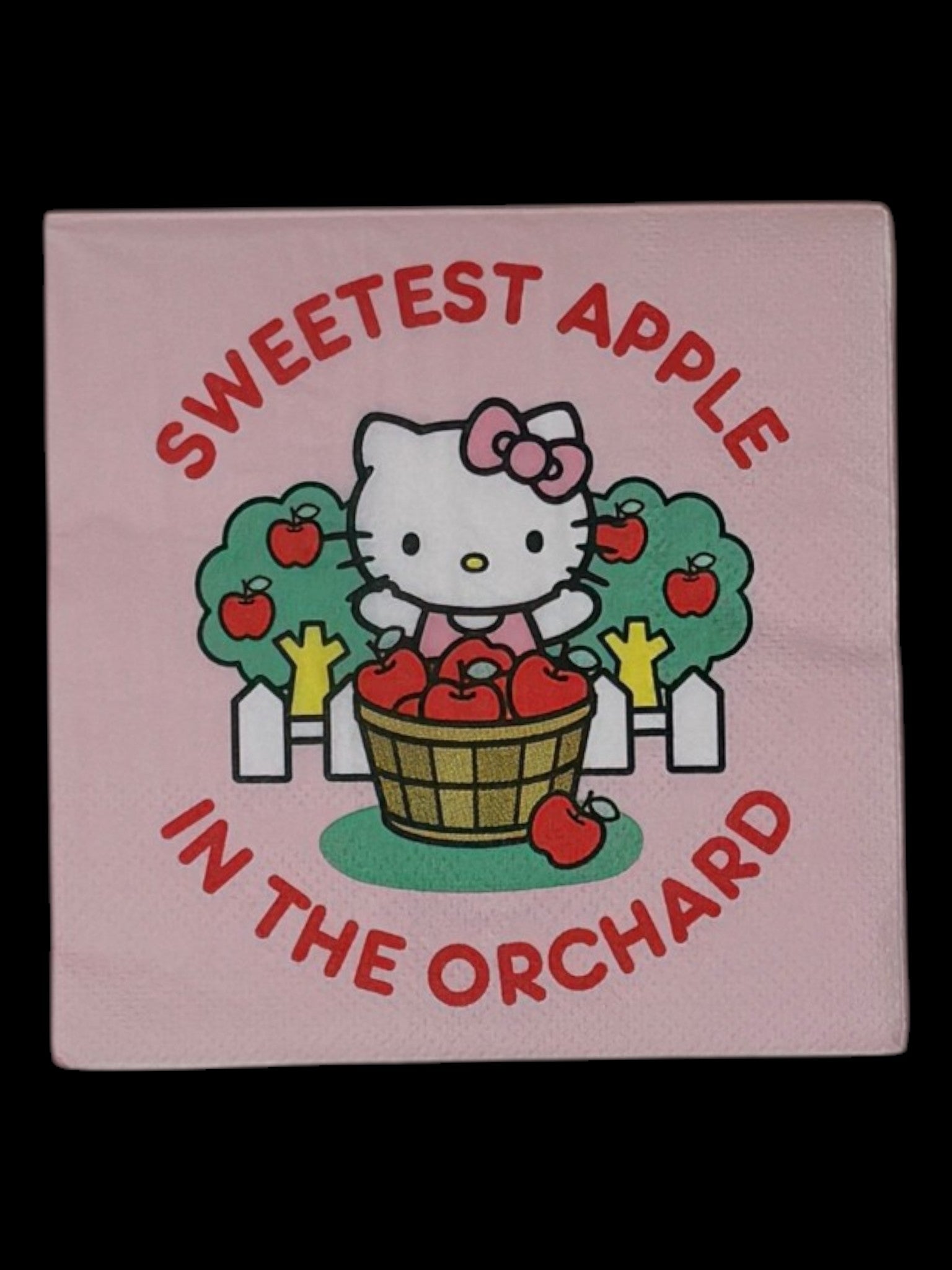 Cocktail-size decoupage paper napkin featuring Hello Kitty standing behind a wooden barrel of red apples with green apple trees and a white picket fence, surrounded by the phrase Sweetest Apple in the Orchard in bold red lettering on a soft blush pink background.