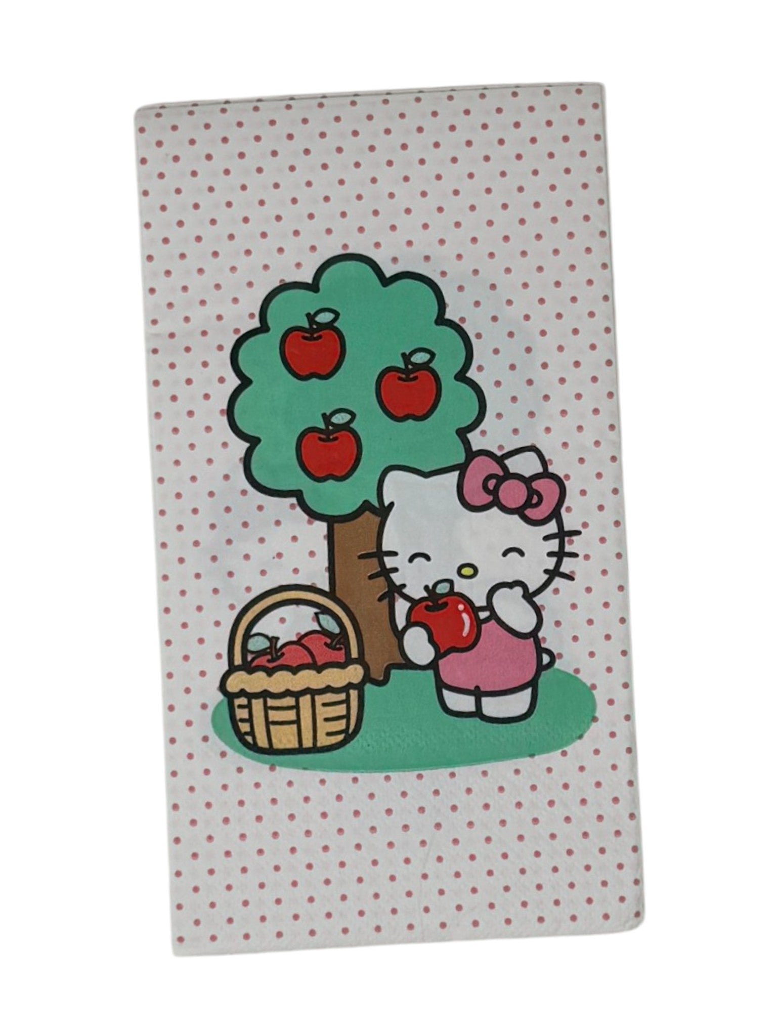 Guest-size decoupage paper napkin featuring a centered illustration of Hello Kitty in a pink bow standing beside a green apple tree with red apples and a wicker basket of apples on a white polka dot background, photographed on a white surface.
