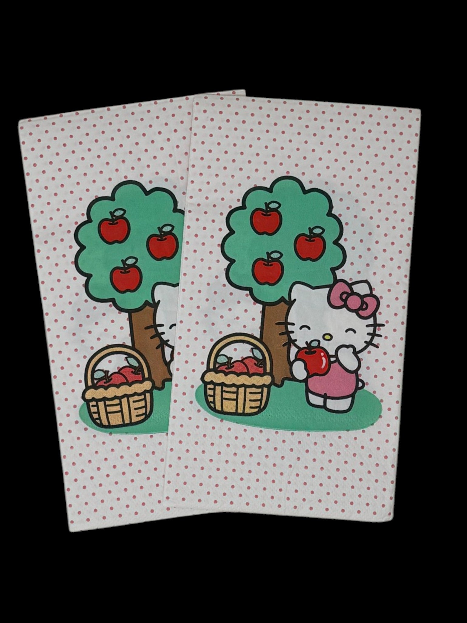 Guest-size decoupage paper napkin featuring a centered illustration of Hello Kitty in a pink bow standing beside a green apple tree with red apples and a wicker basket of apples on a white polka dot background, photographed on a white surface.
