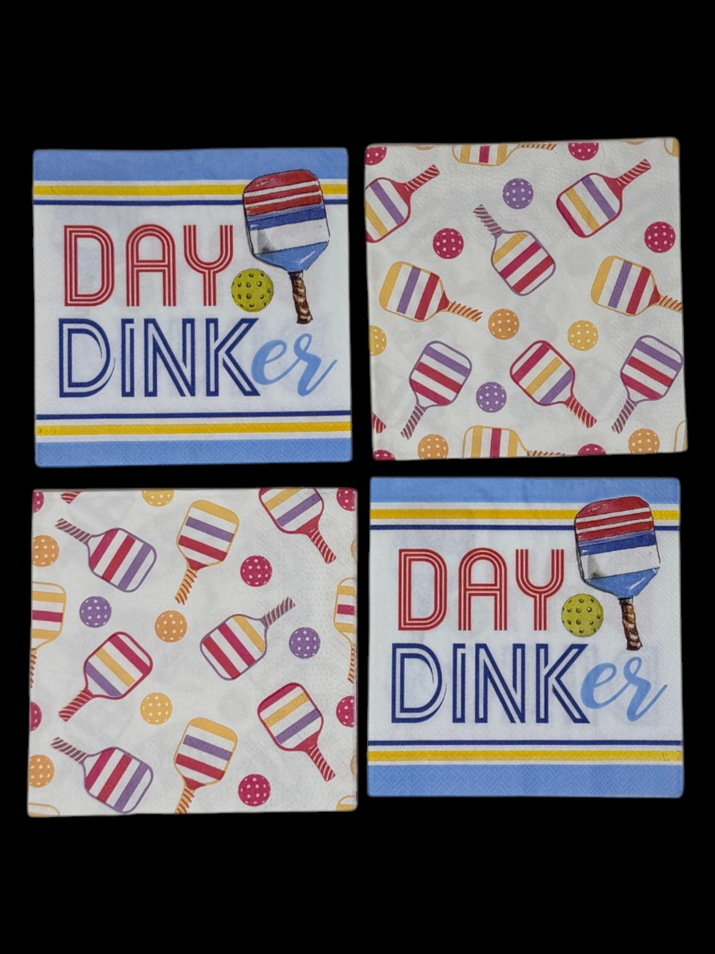 
A bundle of four cocktail-size pickleball themed decoupage paper napkins showing two Day Dinker graphic napkins with bold lettering and a striped paddle on a blue and yellow stripe ground and two colorful all-over tossed paddle and ball pattern napkins on white, photographed on a black surface.