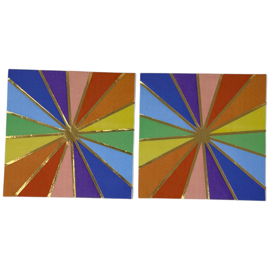 Luncheon-size decoupage paper napkin featuring a bold kaleidoscope pattern of four radiating starburst medallions in cobalt blue, purple, coral, burnt orange, golden yellow, green, and blush pink with crisp white lines and a gold foil starburst accent, photographed unfolded on a light grey surface.