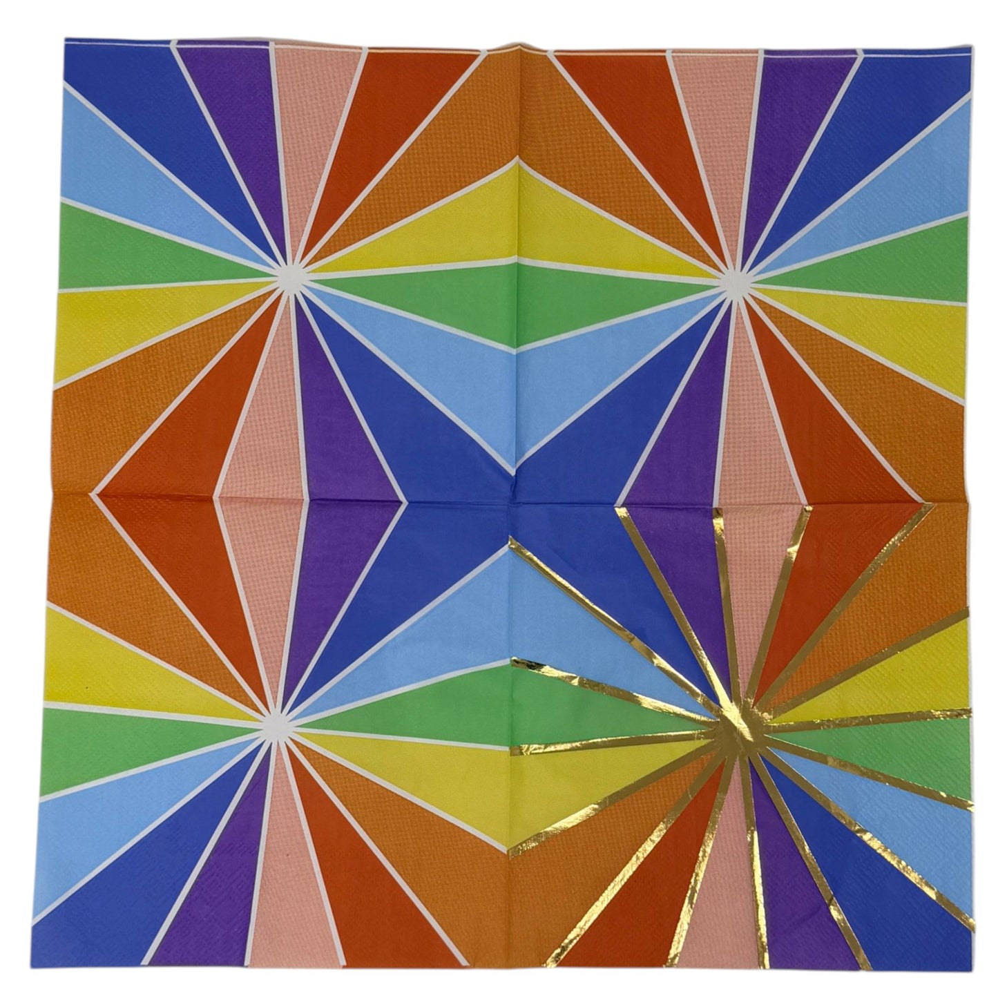 Luncheon-size decoupage paper napkin featuring a bold kaleidoscope pattern of four radiating starburst medallions in cobalt blue, purple, coral, burnt orange, golden yellow, green, and blush pink with crisp white lines and a gold foil starburst accent, photographed unfolded on a light grey surface.