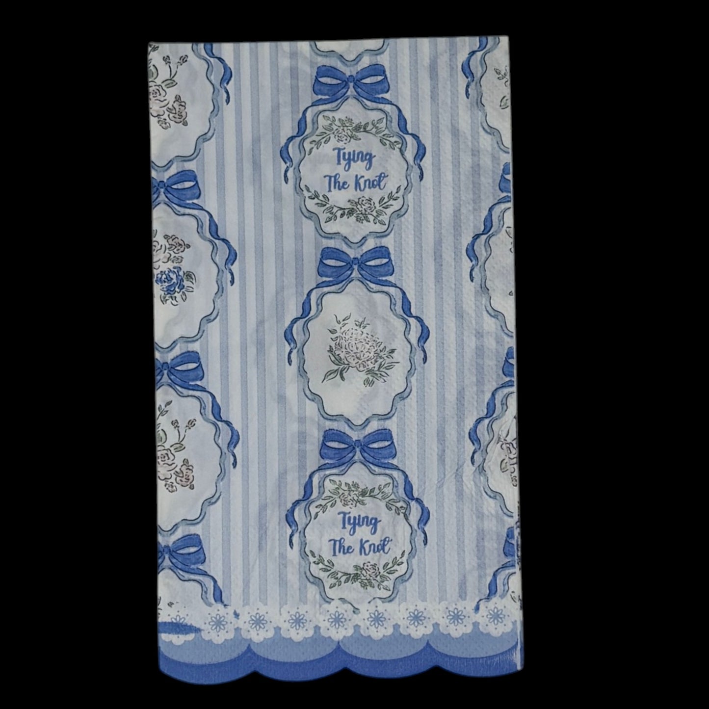 Guest-size decoupage paper napkin featuring a repeating Tying The Knot phrase in elegant script inside an ornate floral cartouche with a blue satin bow on a soft blue and white vertical stripe ground with a scalloped lace border edge, photographed on a black surface.