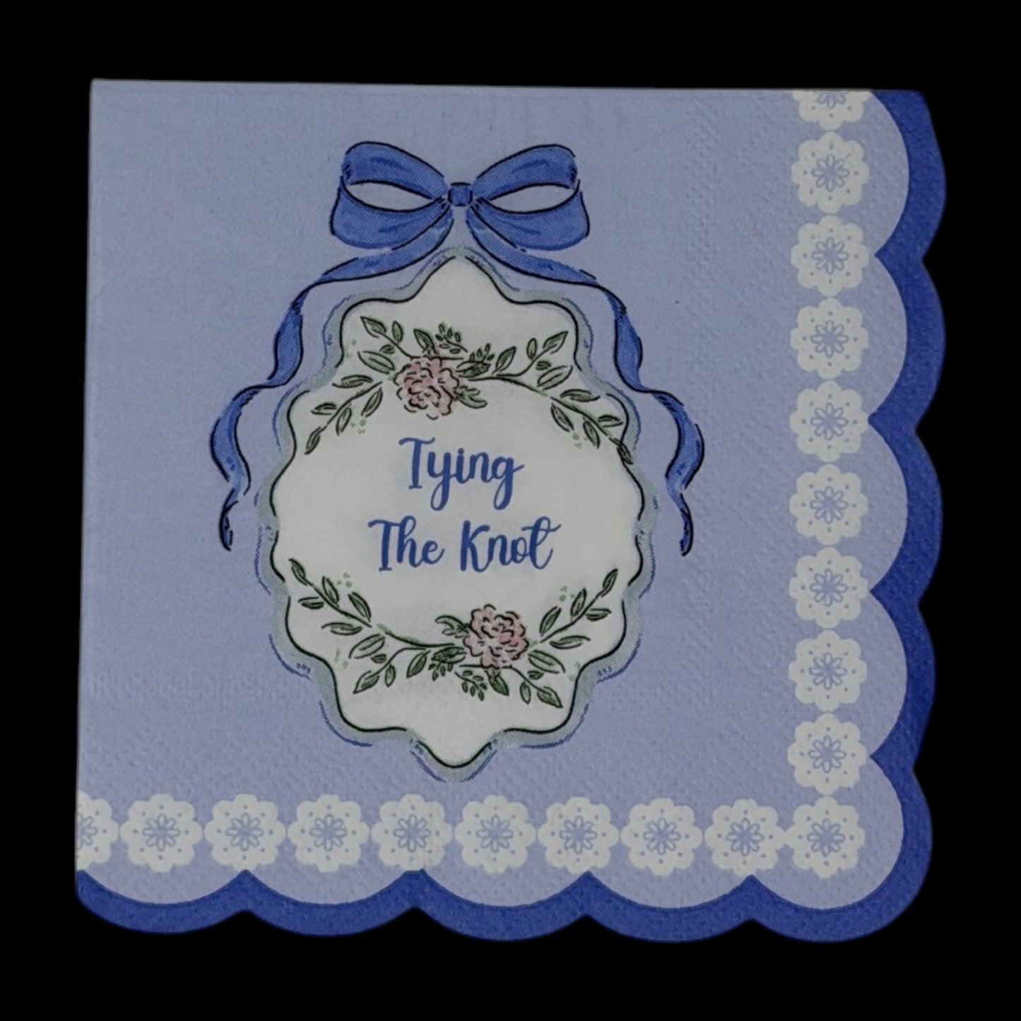 Cocktail-size decoupage paper napkin featuring a centered Tying The Knot medallion with elegant script inside an ornate floral cartouche with a blue satin bow on a solid periwinkle blue ground with a white daisy scalloped lace border edge, photographed on a black surface.