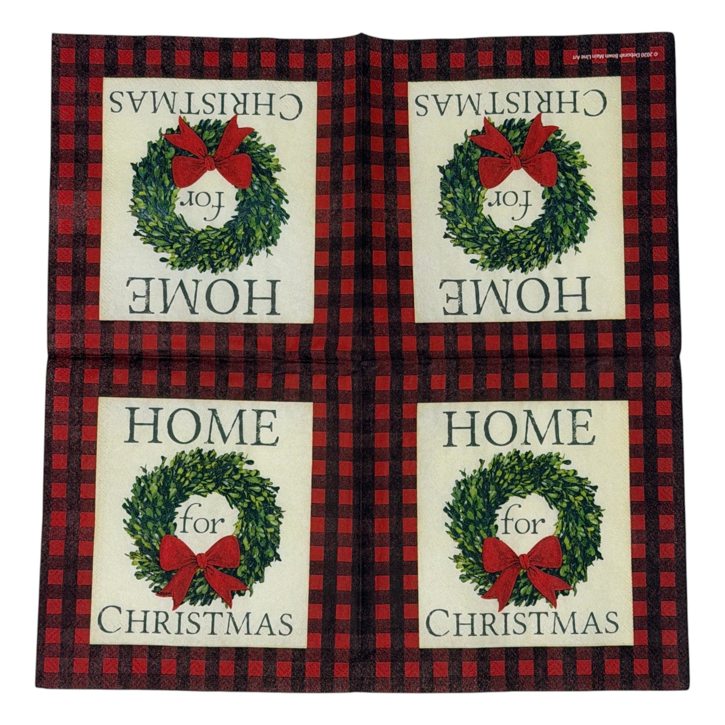 Cocktail-size decoupage paper napkin featuring the phrase Home for Christmas in dark green serif lettering surrounding a lush green boxwood wreath with a full red satin bow on a soft cream ground framed by a deep red and black buffalo check plaid border, photographed on a white surface.