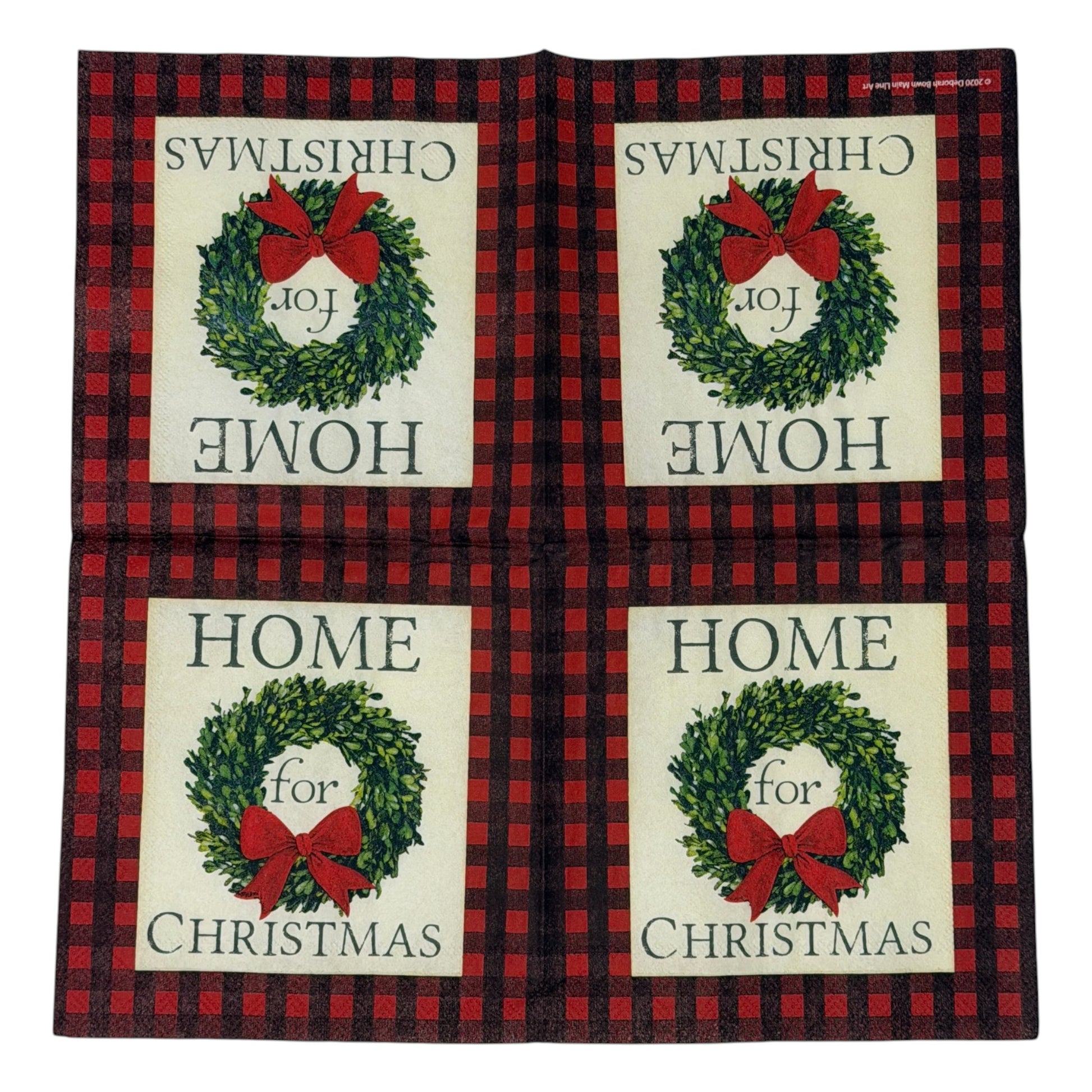 Cocktail-size decoupage paper napkin featuring the phrase Home for Christmas in dark green serif lettering surrounding a lush green boxwood wreath with a full red satin bow on a soft cream ground framed by a deep red and black buffalo check plaid border, photographed on a white surface.