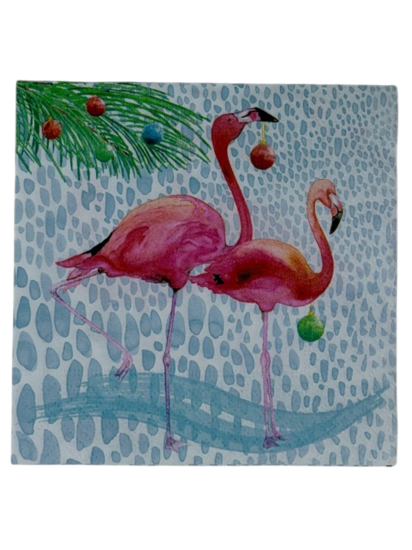 Cocktail-size decoupage paper napkin featuring two watercolor pink flamingos holding colorful Christmas ornaments beneath a pine branch decorated with holiday balls in red teal orange and green on a soft white pebble textured background, photographed on a white surface.