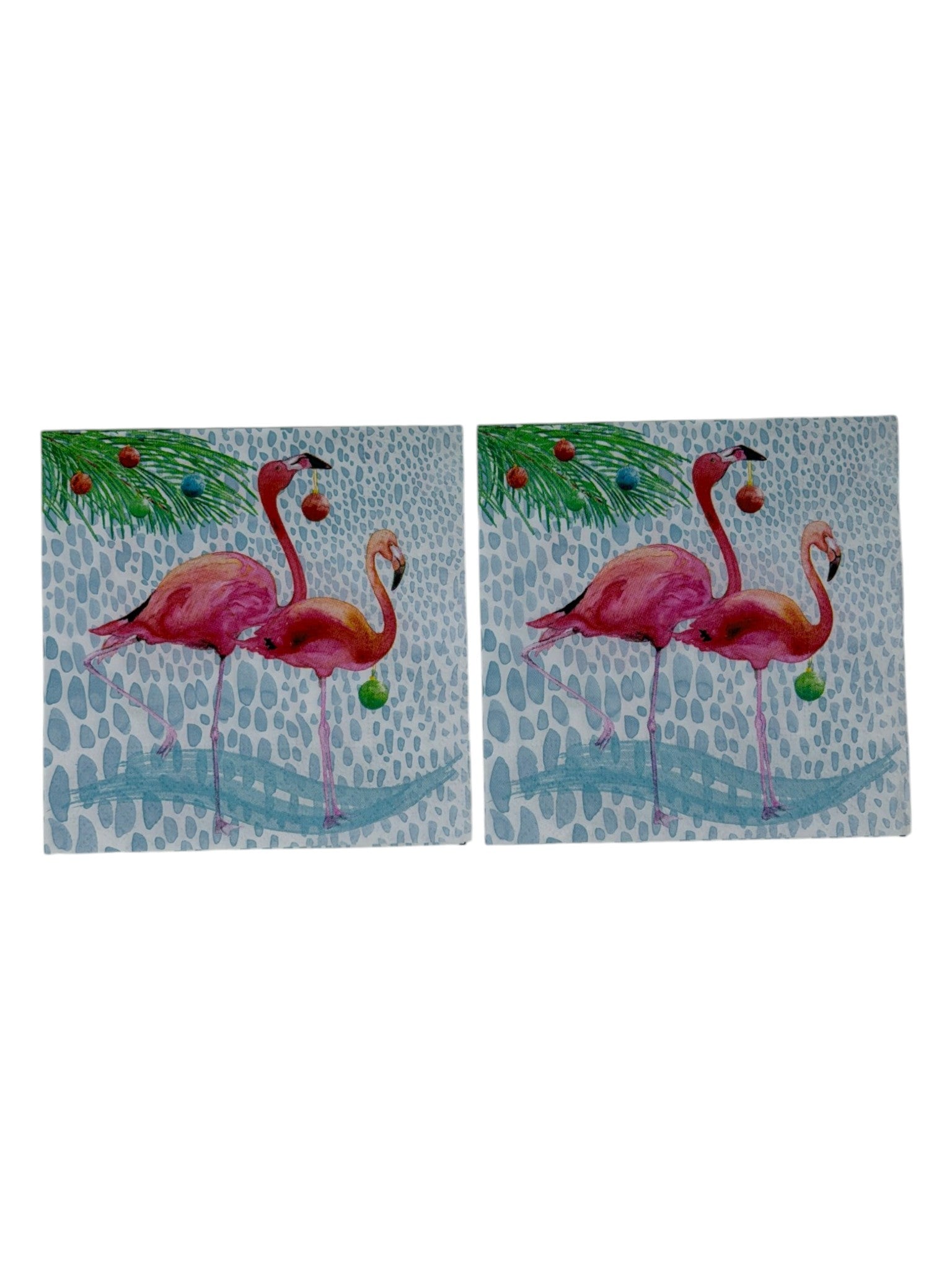 Cocktail-size decoupage paper napkin featuring two watercolor pink flamingos holding colorful Christmas ornaments beneath a pine branch decorated with holiday balls in red teal orange and green on a soft white pebble textured background, photographed on a white surface.