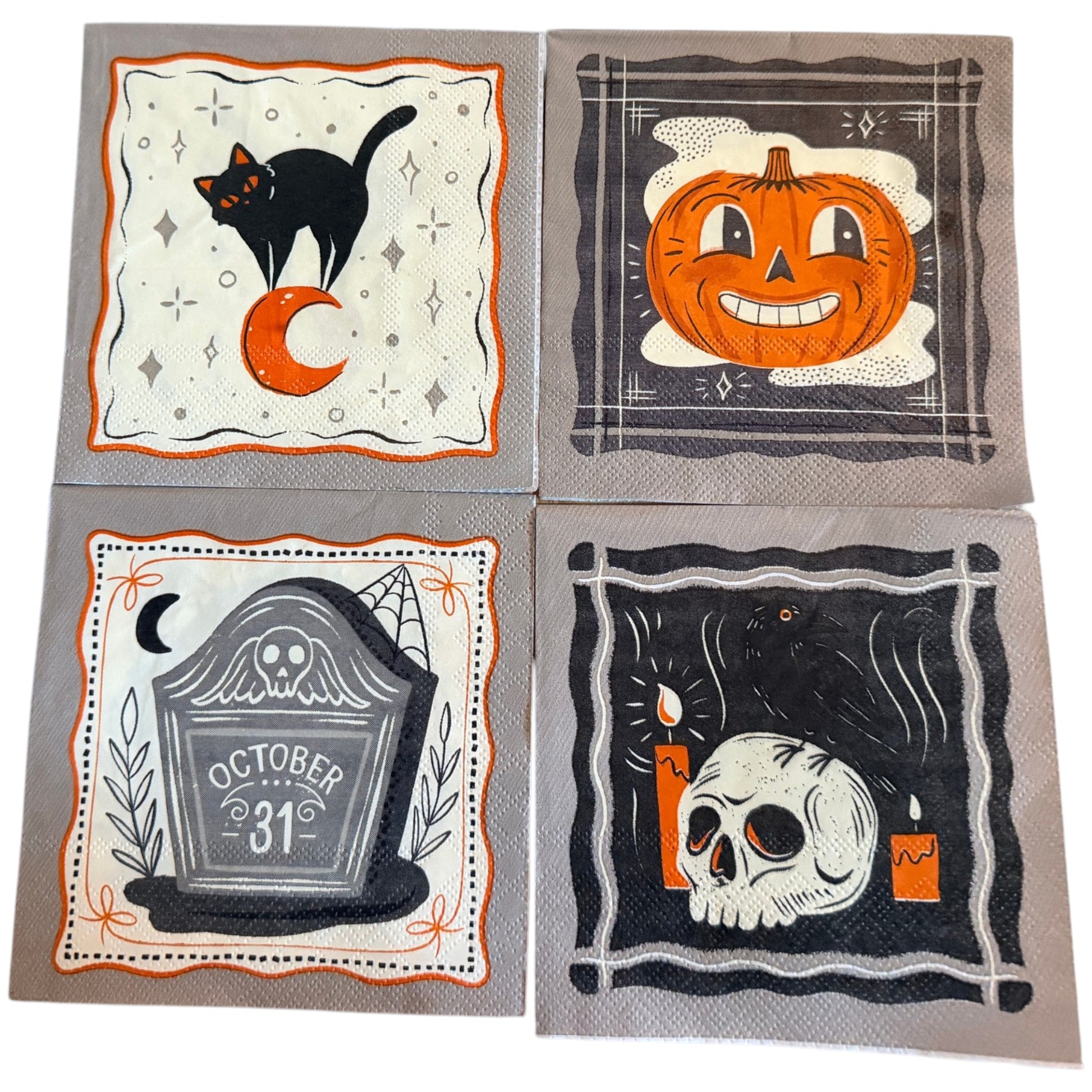 Four square Halloween-themed paper napkins arranged in a 2x2 grid. The designs feature a black cat on a crescent moon, a smiling orange jack-o'-lantern, a tombstone reading 'October 31' with a skull, and a skull with candles against dark backgrounds.